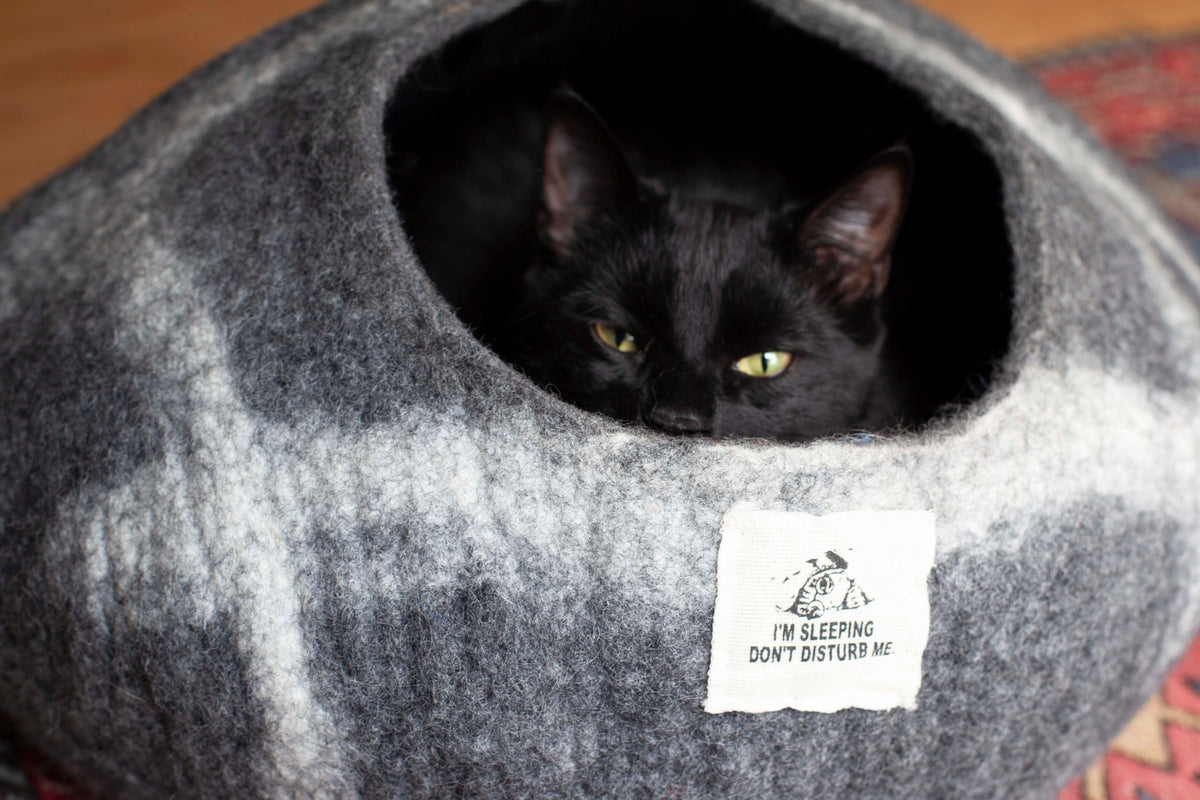 Black cat resting inside grey wool cat cave with I'm sleeping don't disturb me tag - handmade merino felt cat bed